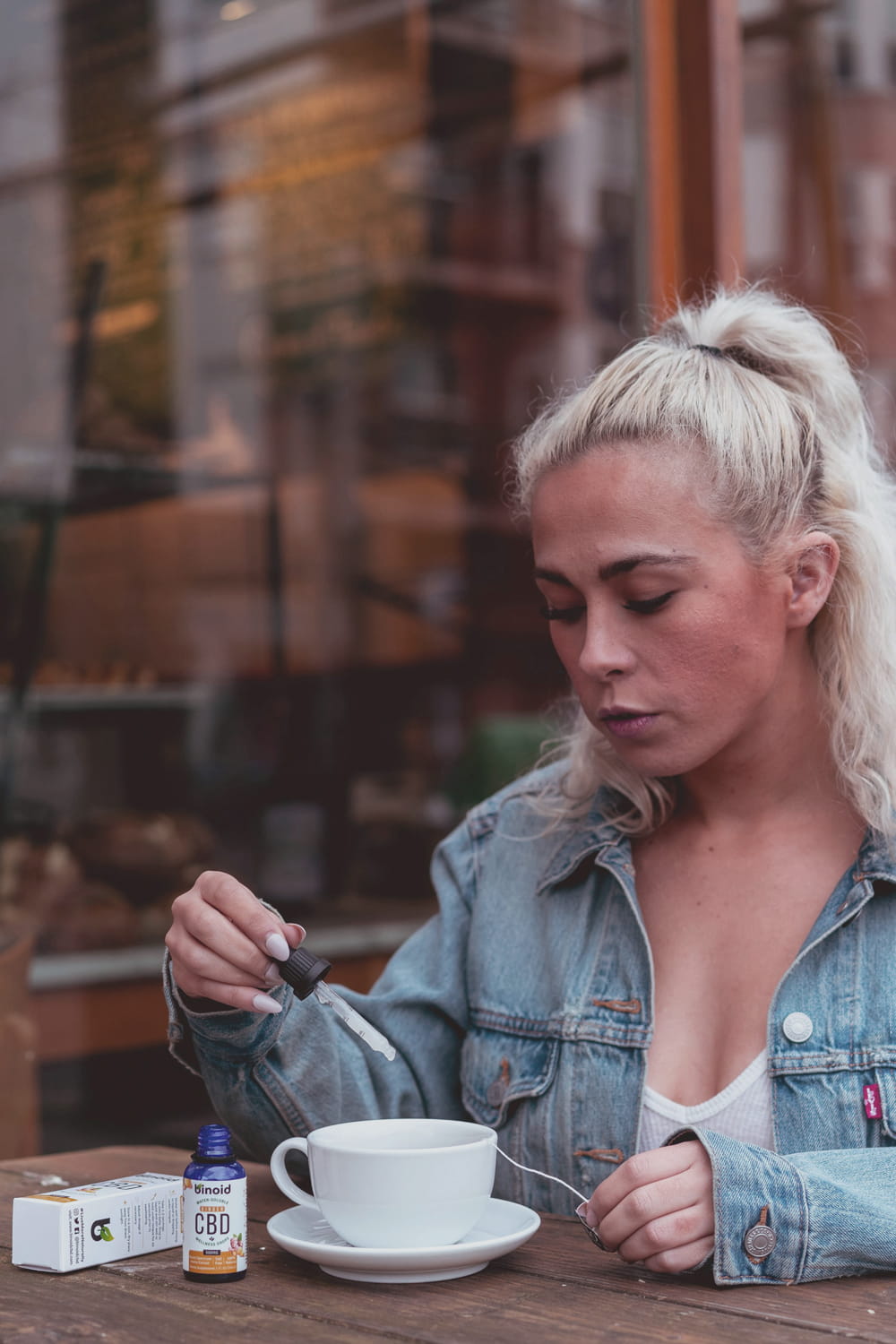 Eine Frau am Tisch nutzt eine Pipette, um CBD Öl in ein Getränk zu geben